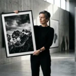 European photographer holding a dramatic black and white print in a gallery setting